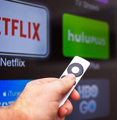 Person holding a Fire Stick remote in front of a smart TV, representing streaming capabilities