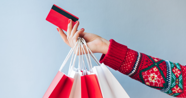 Person holding a credit card and shopping bags, wearing a festive Christmas sweater