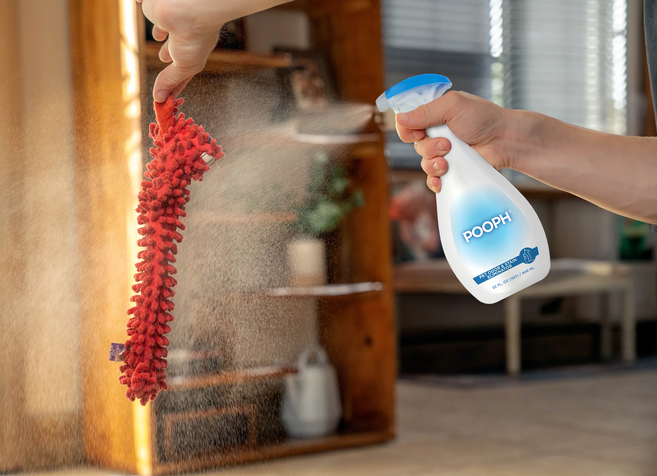 Pooph odor eliminator spray being used on a red dog toy to remove pet odors