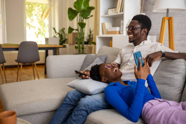 Two people on a couch, one watching TV and the other using a smartphone, representing multi-screen media consumption