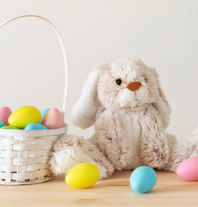 Easter toy bunny, colored eggs with basket on wooden table with white background and copy space.