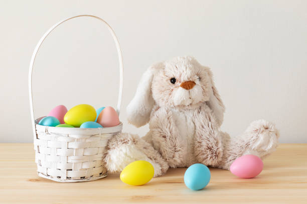 Easter toy bunny, colored eggs with basket on wooden table with white background and copy space.